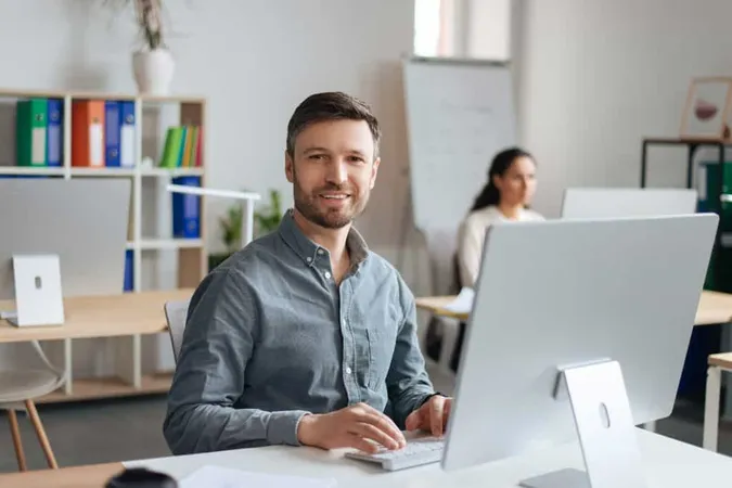 Handsome Cheerful Man Sitting Desk Using Modern Computer Open Space Office X - Atlassian Certified Professional study guide