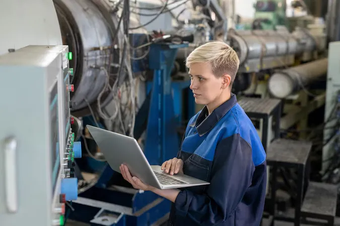 Young Serious Blond Female Worker Overalls Using Laptop While Looking Through Online Technical Data Against Industrial Equipment Workshop - Certified Control Systems Technician study guide
