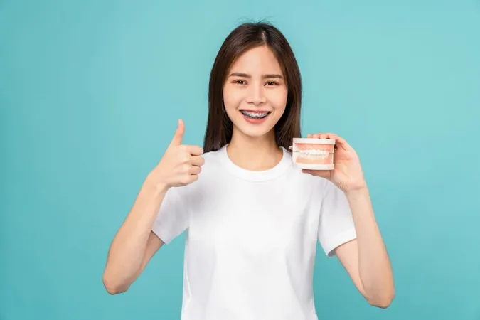 Smiling Asian Woman Wearing Braces Showing Thumbs Up Like Holding Tooth Model Blue Background Concept Oral Hygiene Health Care X - Certified Orthodontic Assistant study guide