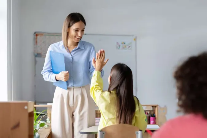 Smiling Caucasian Female Teacher Giving High Five Schoolgirl Sitting Desk Education Childhood X - Certified Out-of-State Teacher study guide