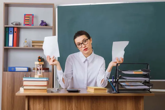 Young Woman Teacher Wearing Glasses Tearing Piece Paper Looking Displeased Sitting School Desk Front Blackboard Classroom X - Certified Out-of-State Teacher study guide