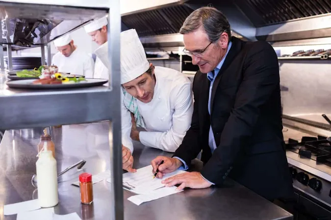 Male Restaurant Manager Writing Clipboard While Interacting Head Chef X - Certified Restaurant Manager study guide