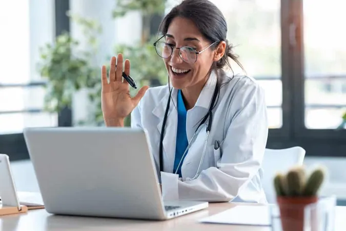 Shot Female Doctor Waving Talking With Colleagues Through Video Call With Laptop Consultation X - Certified Telehealth Coordinator study guide