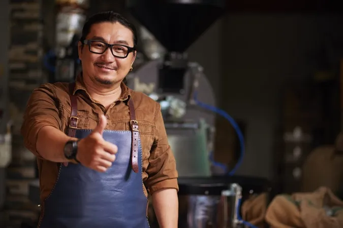 Middle Aged Asian Man Posing With Thumb Up Front Coffee Roasting Equipment X - Master Brewer Certification study guide