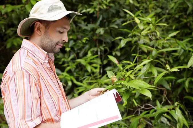 Handsome Botanist With Stubble Wearing Striped Shirt Holding Manual Guide One Hand Green Plant With Flowers Another Studying Its Characteristics With Happy Joyful Look X - PCO Organic Contract Inspector Certified study guide