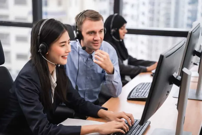 Happy Smiling Asian Woman Call Center Operator With Colleague Wearing Headsets Working Computer Talking With Customer With Her Service Mind X - Service Desk Institute Certifications study guide
