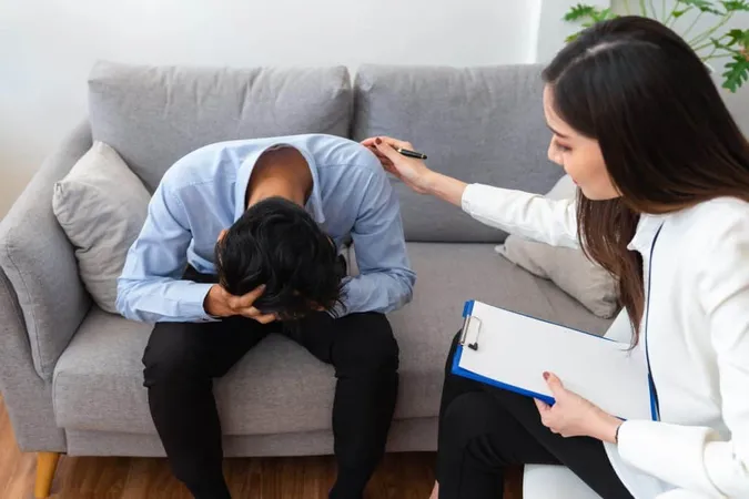 Stressed Asian Young Man Patient Have Life Problem Sitting Sofa With Hands Holding His Head While Woman Psychiatrist Trying Console Him X - Trauma Treatment Certification study guide